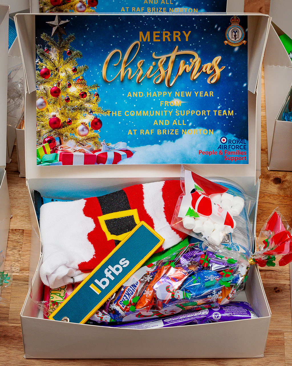 A photo of an open Christmas box, before gift wrapping, showing its contents, which consisted sweets, Cristmas hat and decorations